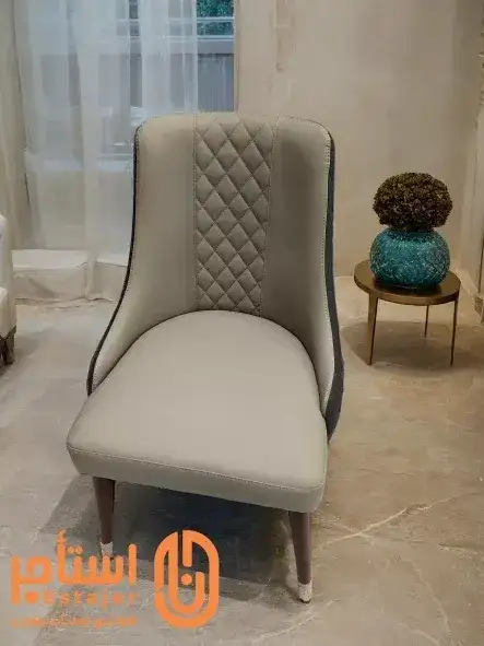 كرسي عصري بتصميم أنيق ومريح ومغطى بجلد فاخر باللون الرمادي،مع تفاصيل منجدة بنمط ماسي على الجزء الخلفي. - الصورة الرئيسية للإيجار | استأجر